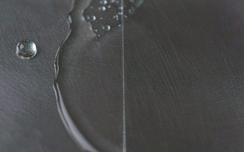 Anti-fingerprint coated brushed stainless steel surface with a beaded water droplet